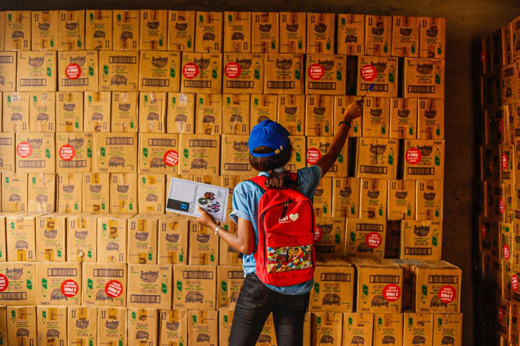 A woman wearing a red backpack and a blue hat working in a warehouse