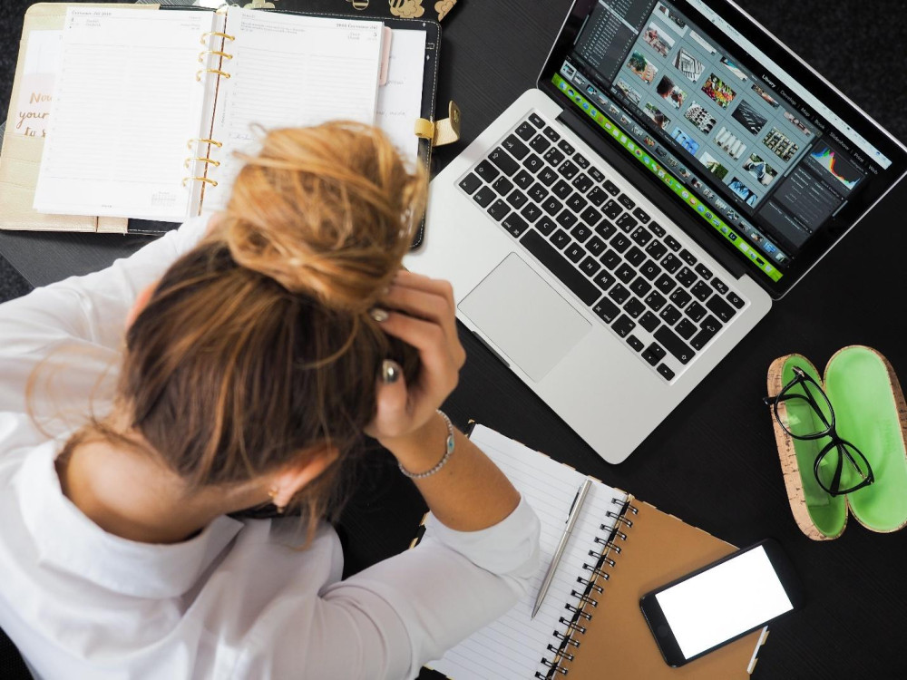 a woman sitting in front of a laptop, holding her head