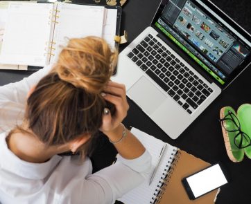 a woman sitting in front of a laptop, holding her head