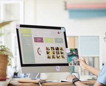 Portrait of young African-American photographer managing photo stock marketplace while using computer at desk in home office with photo website on screen, copy space